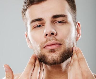 Un hombre con barba recortada se toca la mandíbula con ambas manos mientras mira directamente a la cámara.